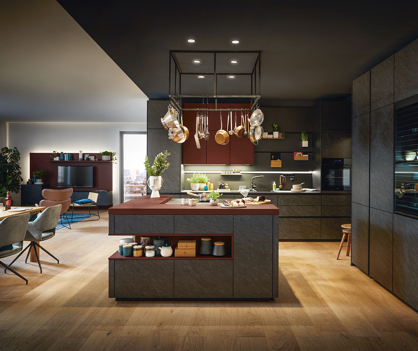 Moderne,&#x20;dunkle&#x20;K&#xFC;che&#x20;mit&#x20;zentraler&#x20;Insel,&#x20;h&#xE4;ngenden&#x20;Kupfert&#xF6;pfen&#x20;und&#x20;offenen&#x20;Regalen.&#x20;Die&#x20;K&#xFC;che&#x20;ist&#x20;in&#x20;dunklen&#x20;Graut&#xF6;nen&#x20;und&#x20;warmem&#x20;Holz&#x20;gestaltet,&#x20;mit&#x20;einem&#x20;Esstisch&#x20;und&#x20;einem&#x20;Wohnzimmer&#x20;im&#x20;Hintergrund.