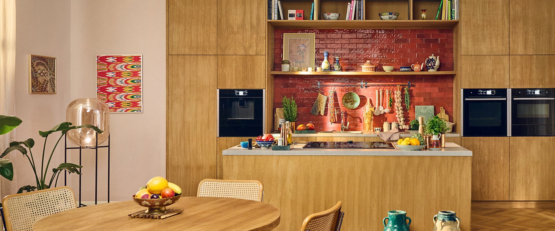 Gem&#xFC;tliche&#x20;K&#xFC;che&#x20;mit&#x20;Holzschr&#xE4;nken,&#x20;roter&#x20;Fliesenr&#xFC;ckwand&#x20;und&#x20;dekorativer&#x20;Kochinsel.&#x20;Bunte&#x20;Kunstwerke&#x20;und&#x20;Keramik&#x20;verleihen&#x20;dem&#x20;Raum&#x20;W&#xE4;rme.