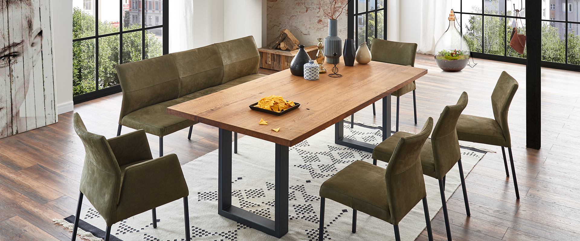 Esszimmer&#x20;mit&#x20;Holztisch,&#x20;gr&#xFC;nen&#x20;Polsterst&#xFC;hlen&#x20;und&#x20;-bank,&#x20;dekoriert&#x20;mit&#x20;Vasen.&#x20;Ein&#x20;Teller&#x20;mit&#x20;Nachos&#x20;steht&#x20;auf&#x20;dem&#x20;Tisch,&#x20;im&#x20;Hintergrund&#x20;gro&#xDF;e&#x20;Fenster.