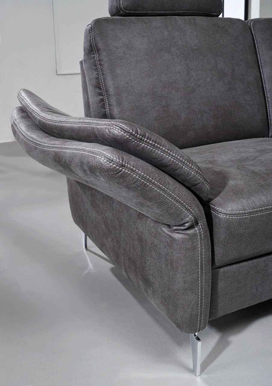Nahaufnahme&#x20;einer&#x20;dunkelgrauen&#x20;Polstersofa-Armlehne&#x20;mit&#x20;geschichteten&#x20;Kissen&#x20;und&#x20;sichtbaren&#x20;N&#xE4;hten,&#x20;gest&#xFC;tzt&#x20;von&#x20;schlanken,&#x20;angewinkelten&#x20;Metallbeinen.