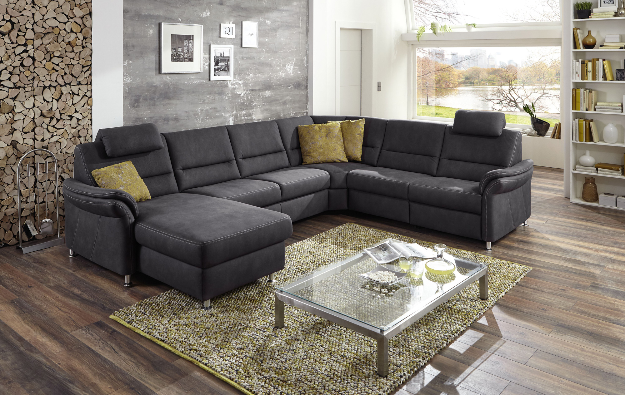 Modernes&#x20;Wohnzimmer&#x20;mit&#x20;grauem&#x20;Ecksofa,&#x20;gelben&#x20;Kissen,&#x20;Glastisch&#x20;auf&#x20;Teppich,&#x20;Holzstapelwand&#x20;und&#x20;gro&#xDF;em&#x20;Fenster&#x20;mit&#x20;Aussicht.