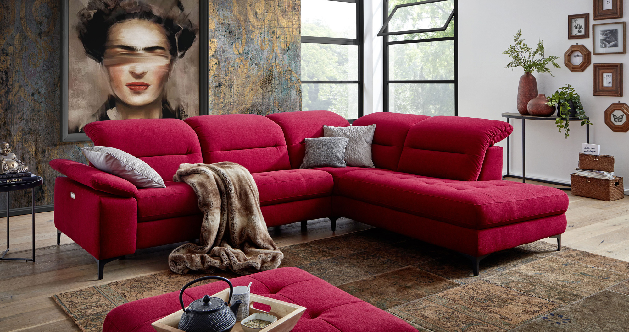 Stilvolles,&#x20;rotes&#x20;Ecksofa&#x20;auf&#x20;gemustertem&#x20;Teppich,&#x20;Wandbildnis&#x20;einer&#x20;Frau,&#x20;Kunstpflanzen&#x20;und&#x20;gro&#xDF;e&#x20;Fenstern